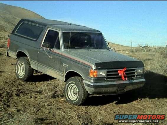1989 Ford Bronco parked on a dirt hill with a red bow on the grille