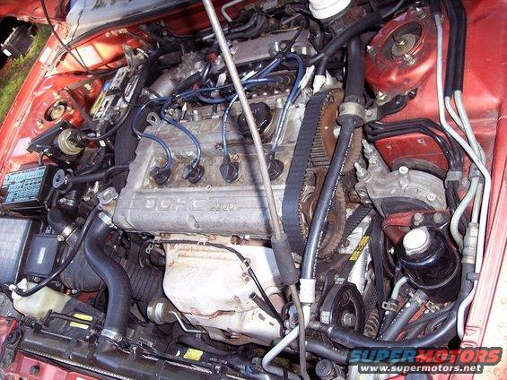Engine bay with DOHC 16V engine visible, hoses, belts, and fuse box