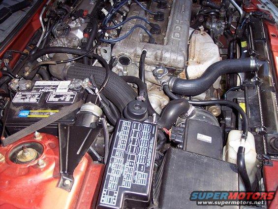 Engine bay with battery, fuse box, and engine components visible. Some hoses and wiring are present