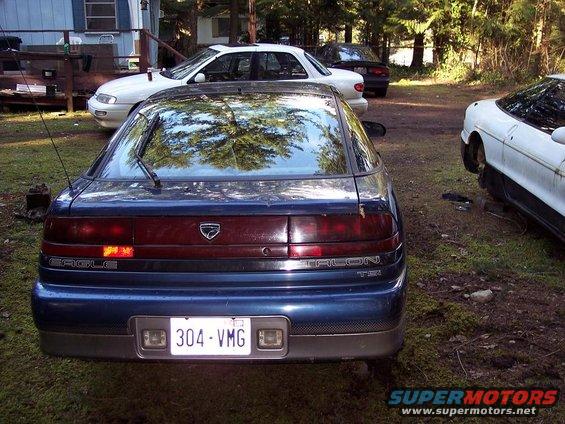 Rear of a blue Eagle Talon TSi with a license plate reading 304-VMG. Other cars are visible in the background