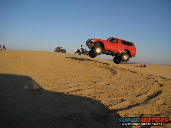 Red SUV airborne over sand dune, front grille guard visible