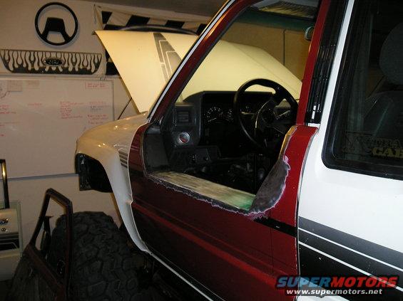 Pickup truck interior with door removed, showing dashboard and steering wheel. Hood is open