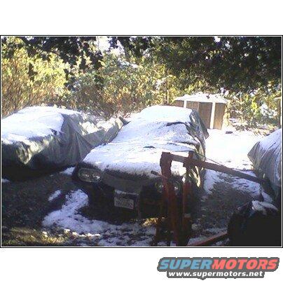 1972 Ford Ranchero covered in snow, front view, with a red engine hoist nearby