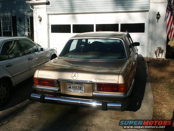Gold Mercedes-Benz sedan parked in front of a garage, another white Mercedes-Benz is to its left