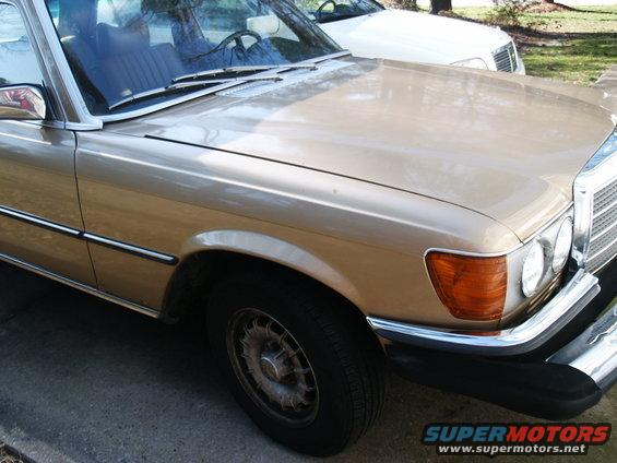 Gold Mercedes-Benz W116 sedan, front passenger side view. Chrome trim, amber turn signal, and alloy wheel visible