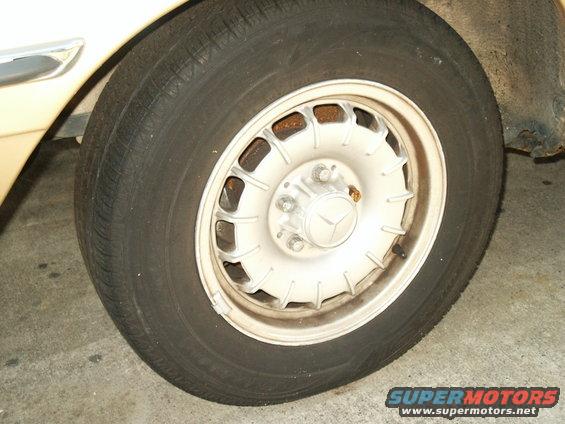 Cream-colored Mercedes-Benz wheel with a Mercedes-Benz logo and a tire. Some rust is visible on the wheel