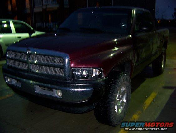 Front 3/4 view of a red Dodge pickup truck. Another white SUV is parked to the left
