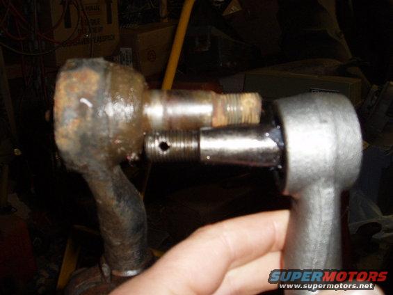 Two rusty and one new tie rod end assembly components, one held by a hand