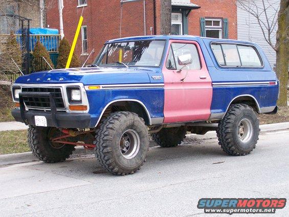 Blue Ford Bronco with a pink door, lifted with large tires