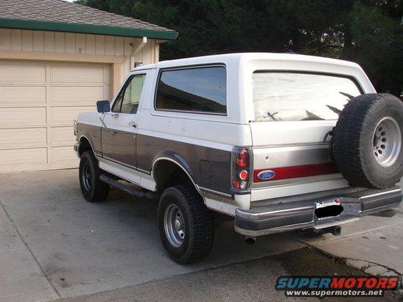1989 Ford Bronco parked in front of a garage, showing the rear passenger side and spare tire
