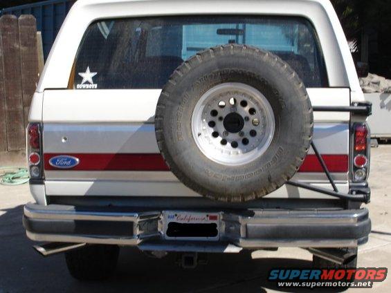 Rear of a white Ford Bronco with a spare tire mounted on the back. Has a red stripe and a Cowboys star sticker