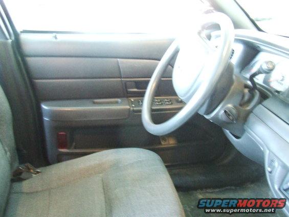 Gray interior of a 2003 Ford Crown Victoria showing the driver's seat, door panel, and steering wheel