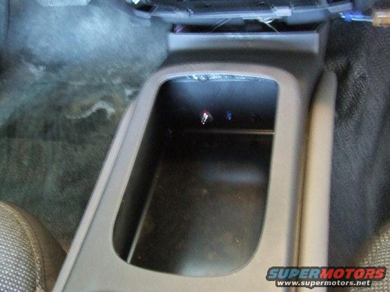 Car interior console with open storage bin and visible wiring