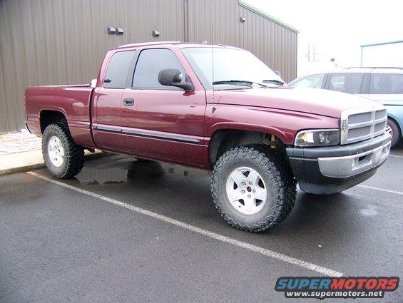 Maroon 2001 Dodge 1500 pickup truck with aftermarket wheels and tires, parked on wet asphalt