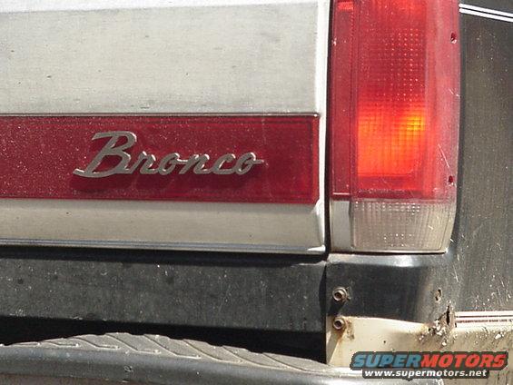 Close-up of a red 'Bronco' badge on a white vehicle, next to a red taillight