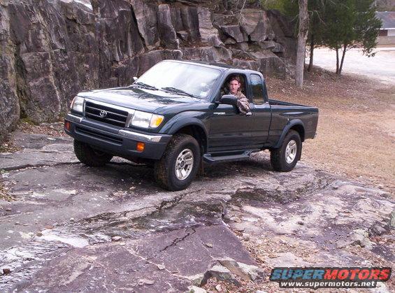 Dark green 1998 Toyota Tacoma pickup truck with a man in the driver's seat, angled on a rocky incline