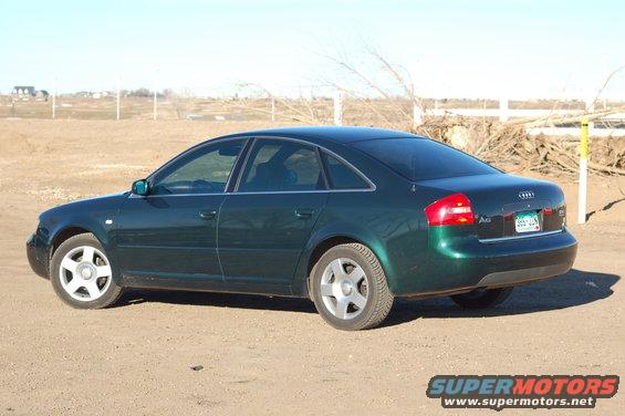 dark green Audi sedan parked on dirt lot, rear quarter view. License plate visible