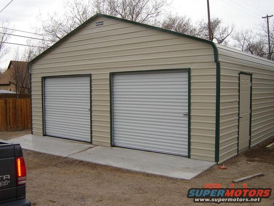 Metal garage with two roll-up doors and a side door. A truck is partially visible in the foreground