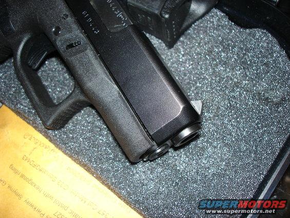 Close-up of a black pistol with a textured grip, resting on a foam surface. Some text is visible on a yellow document underneath