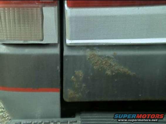 Close-up of rust on the lower rear panel of a vehicle, next to the taillight