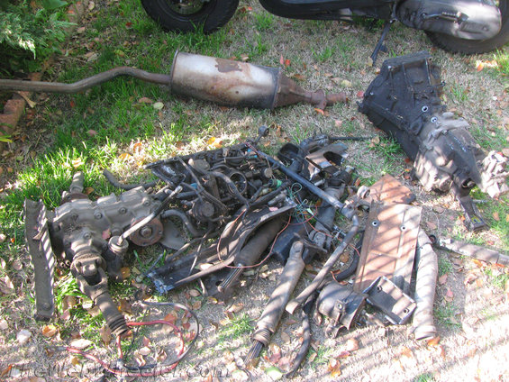 Pile of car parts including engine, transmission, exhaust, and axles on the ground