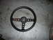 1975 Ford Ranchero - A black steering wheel with a three-spoke design, circular cutouts on the spokes, is shown against a concrete floor.