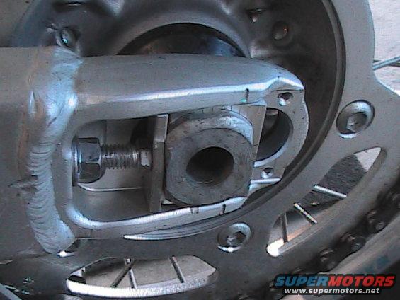 Close-up of a motorcycle's rear axle adjustment bolt and chain