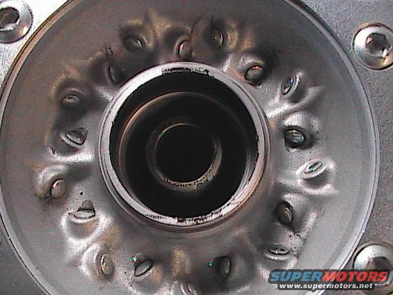 Close-up of a metal part with a central opening and a ring of bolts
