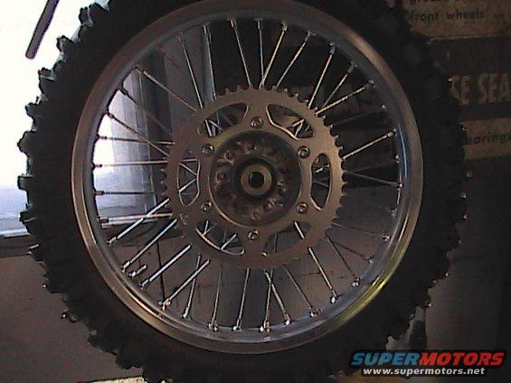Motorcycle rear wheel with knobby tire and silver sprocket, close-up
