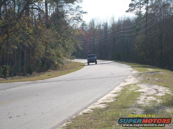 Dark SUV drives on a paved road through a wooded area