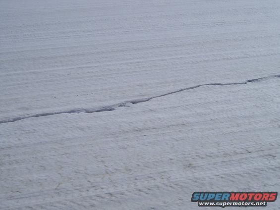snowy field with tire tracks and a crack in the snow