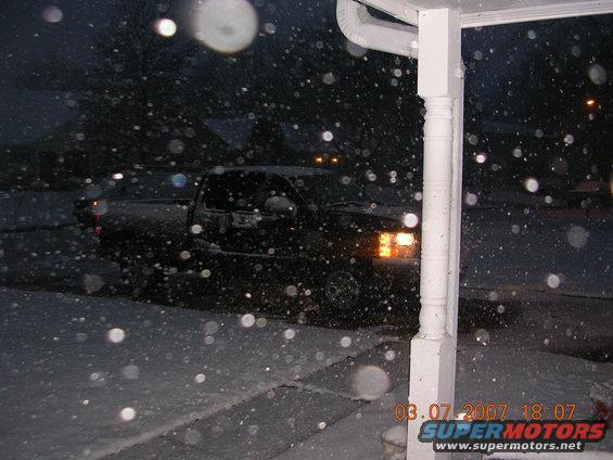 Black pickup truck parked outside during a snowstorm. Date stamp shows 03.07.2007