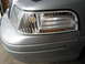 2004 Ford Crown Victoria - Close-up of a silver car's front corner, highlighting the clear turn signal and ribbed headlight assembly.