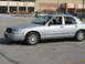 2004 Ford Crown Victoria - A silver 2004 Ford Crown Victoria is parked in a lot with a building in the background.