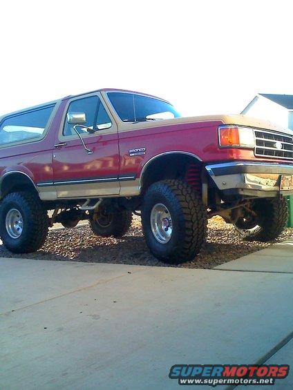 Red and tan lifted Ford Bronco with large tires parked on gravel