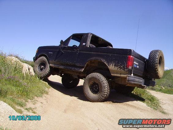 Black SUV with lifted suspension and large tires driving off-road. Spare tire mounted on the back