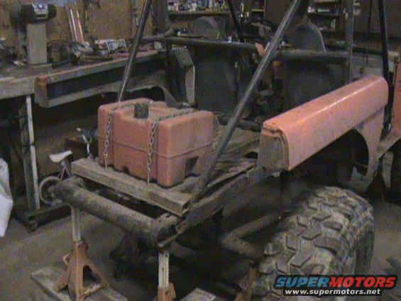 Off-road vehicle with orange auxiliary fuel tank chained to a wooden platform, rear view