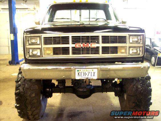 Front view of a lifted GMC pickup truck with large off-road tires and a chrome bumper. The GMC logo is visible on the grille