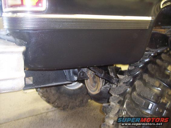 Black pickup truck rear fender and large off-road tire, showing leaf springs and part of a taillight