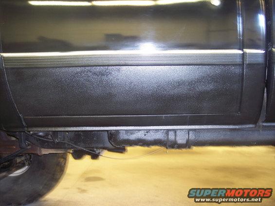Side view of a black truck's lower body panel and frame. Shows a textured lower section with a chrome trim strip above it