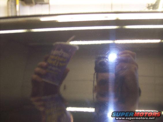 Reflection of a person holding a cup and a camera in a dark, reflective surface