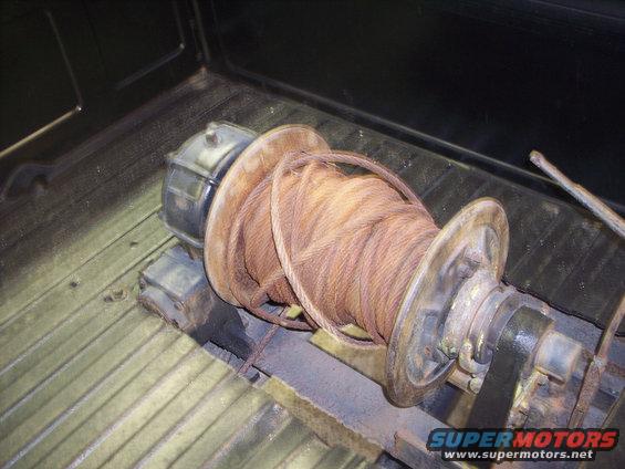 Winch with rusty cable coiled on spool, mounted in the bed of a truck