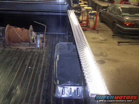 Truck bed interior showing a rusty winch on the left and a diamond plate toolbox on the right