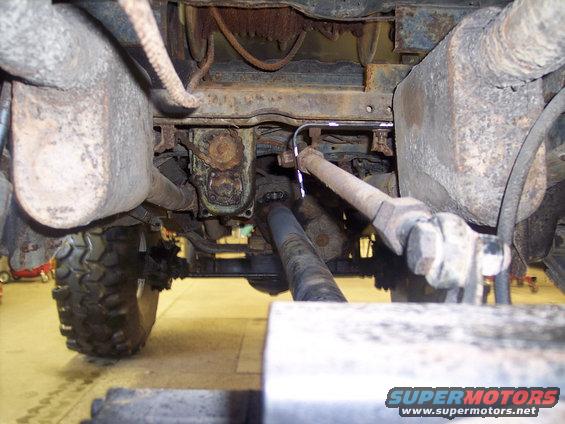 Undercarriage of a heavily rusted truck, showing suspension components, exhaust system, and a tire