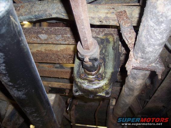 Underside view of a vehicle's steering box and linkage, showing rust and grease