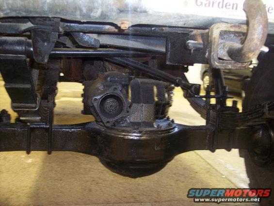 Underside view of a vehicle's rear axle, leaf springs, and driveshaft. A tow hitch is visible