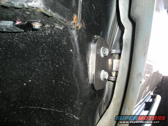 Door hinge mounting plate bolted to black undercarriage with rust visible