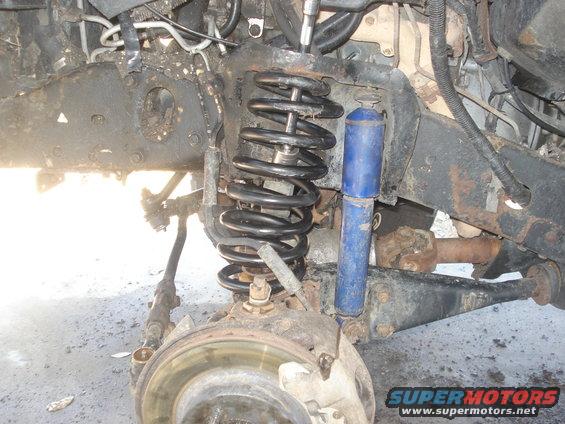 close-up of a vehicle's front suspension with coil spring and blue shock absorber