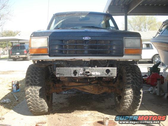 1989 Ford Bronco II front view, lifted with aftermarket bumper and large tires. Another SUV and a boat are visible in the background