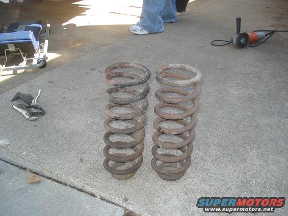 Two rusty coil springs on concrete, with tools and a creeper nearby
